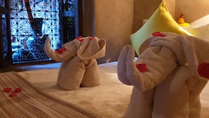 Ein plüschiger Elefant und ein plüschiger Hase liegen auf einem Bett mit Rosenblättern, mit einem Zierfenster und einem gelben Kissen.