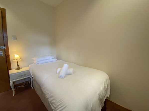 Une chambre d’hôtel avec un lit simple, une table de chevet avec une lampe et une porte.