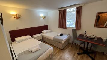 Habitación de hotel con dos camas, un escritorio y una silla. Hay lámparas de pared y una ventana con cortinas.