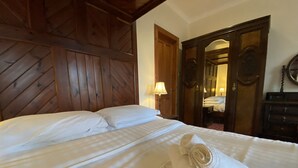 Une chambre d’hôtel avec une tête de lit en bois, un lit bien fait avec du linge de lit blanc, une serviette roulée posée sur le lit et une armoire en bois avec un miroir.