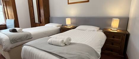 A hotel room with two beds, a wooden wardrobe, a framed picture on the wall, and bedside lamps.