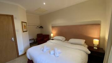 Una habitación de hotel con una cama grande, dos lámparas de noche, un sillón rojo y una mesita con lámpara.