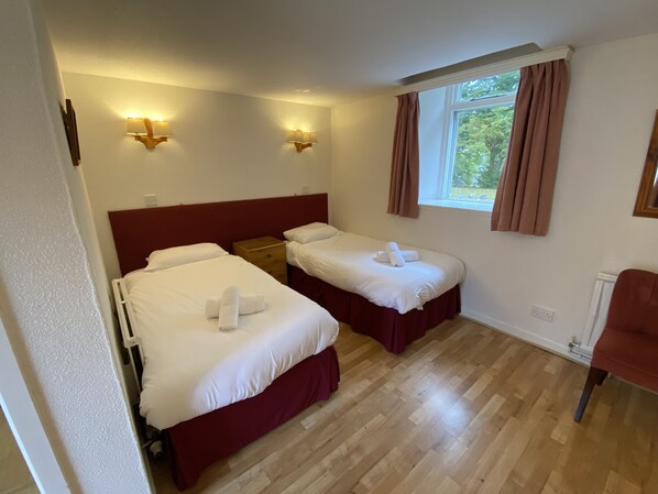 Une chambre d’hôtel avec deux lits, un plancher en bois, une fenêtre avec des rideaux et des lampes fixées au mur.