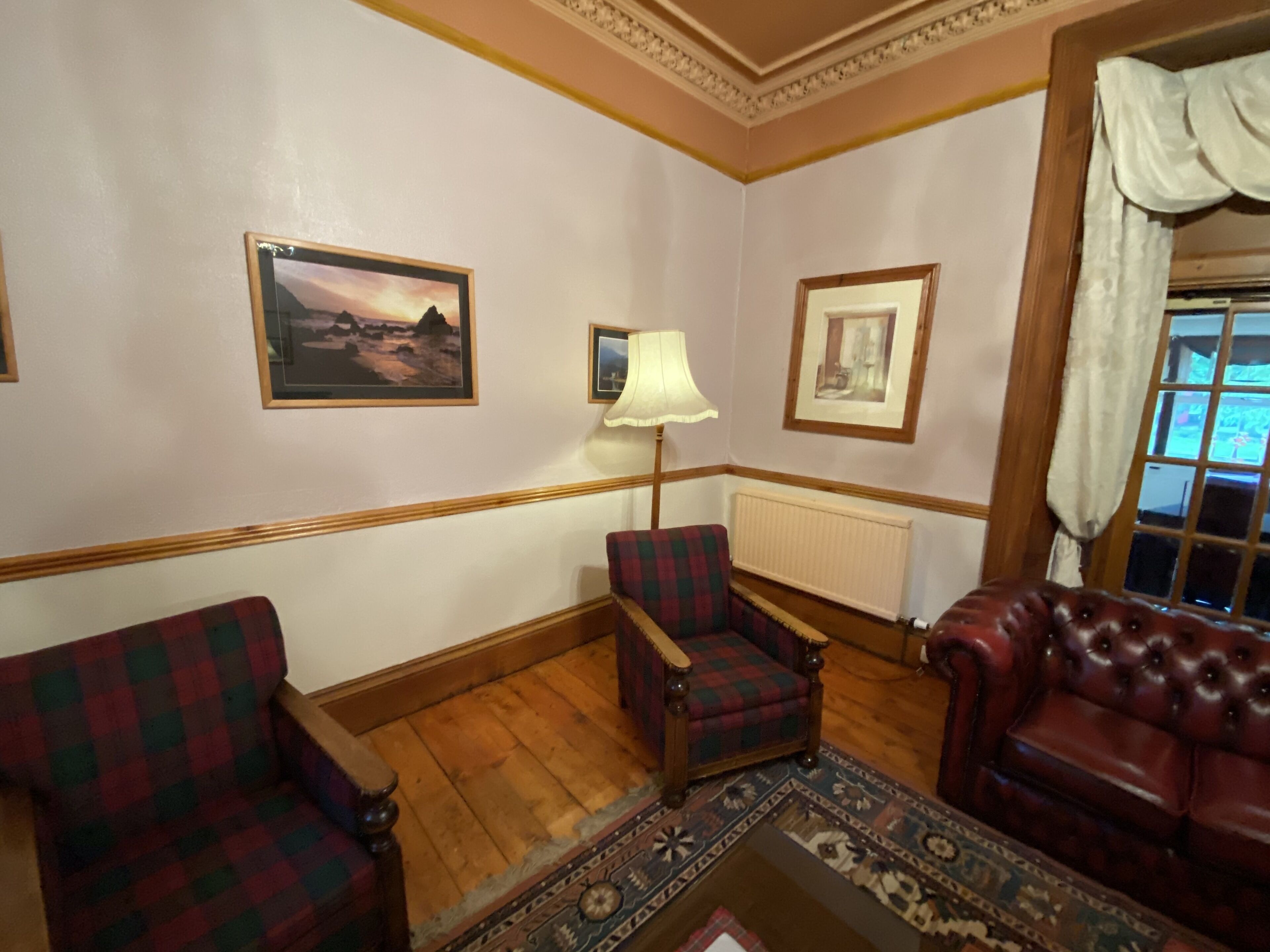 A room with a wooden floor, a plaid armchair, a leather sofa, and a patterned rug.