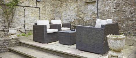 A patio with wicker furniture, stone steps, and a stone wall.