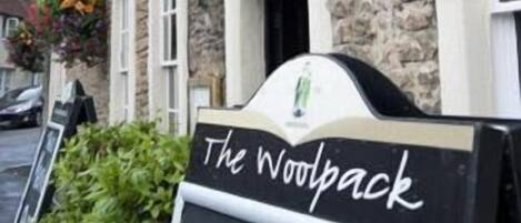 A traditional stone building with flower boxes and a sign reading "The Woolpack Delicacies Traditions".