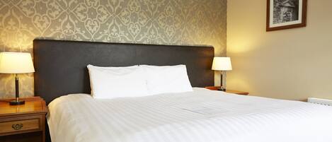 A neatly made bed with white linens, two bedside lamps, and a patterned wallpaper.