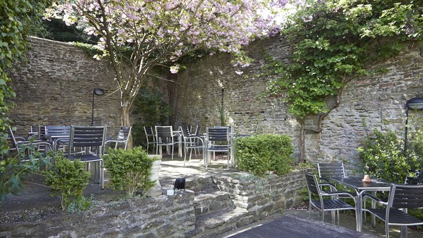 An outdoor patio with stone walls, metal chairs, and tables. - Woolpack Inn Beckington by Greene King Inns (Frome)