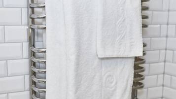 A bathroom with white tiled walls and a chrome towel rack holding two white towels.
