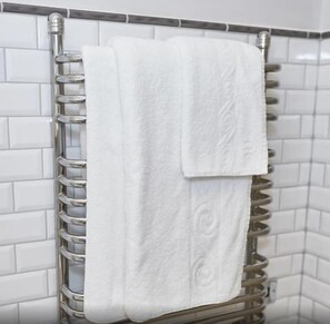 Une salle de bain aux murs recouverts de carreaux blancs et dotée d’un porte-serviettes chromé sur lequel sont posées deux serviettes blanches.