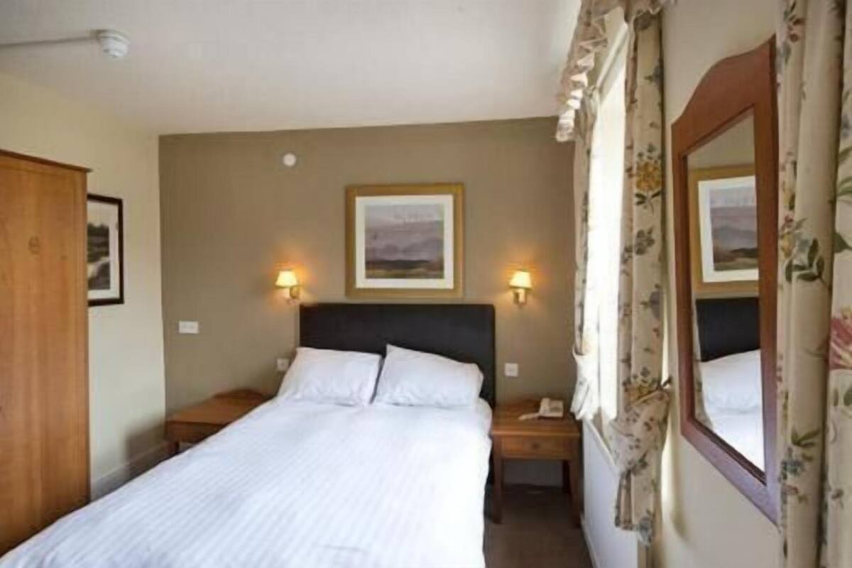 Ein Hotelzimmer mit einem Bett, zwei Nachttischlampen, einem Nachttisch, einem Spiegel und einem gerahmten Bild an der Wand.