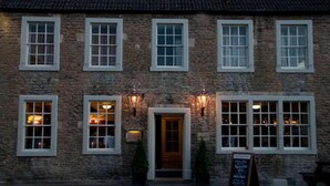 A stone building with multiple windows and a door, featuring a signboard outside. - Woolpack Inn Beckington by Greene King Inns (Frome)