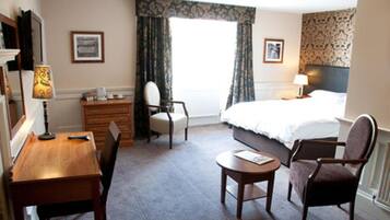 Une chambre d’hôtel comprenant un lit, un bureau, une chaise, une petite table, une commode et une lampe.