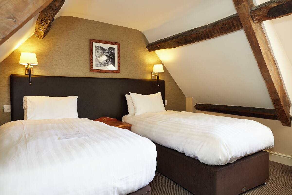 Ein Hotelzimmer mit zwei Betten, Holzbalken und zwei Wandleuchten.