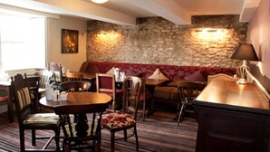 A cozy hotel room with a stone wall, a red sofa, a wooden dining table, and a lamp. - Woolpack Inn Beckington by Greene King Inns (Frome)