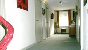 A hallway with white walls, a red spiral staircase on the left, and a door with an exit sign. - Hotel Cobut (Onhaye)