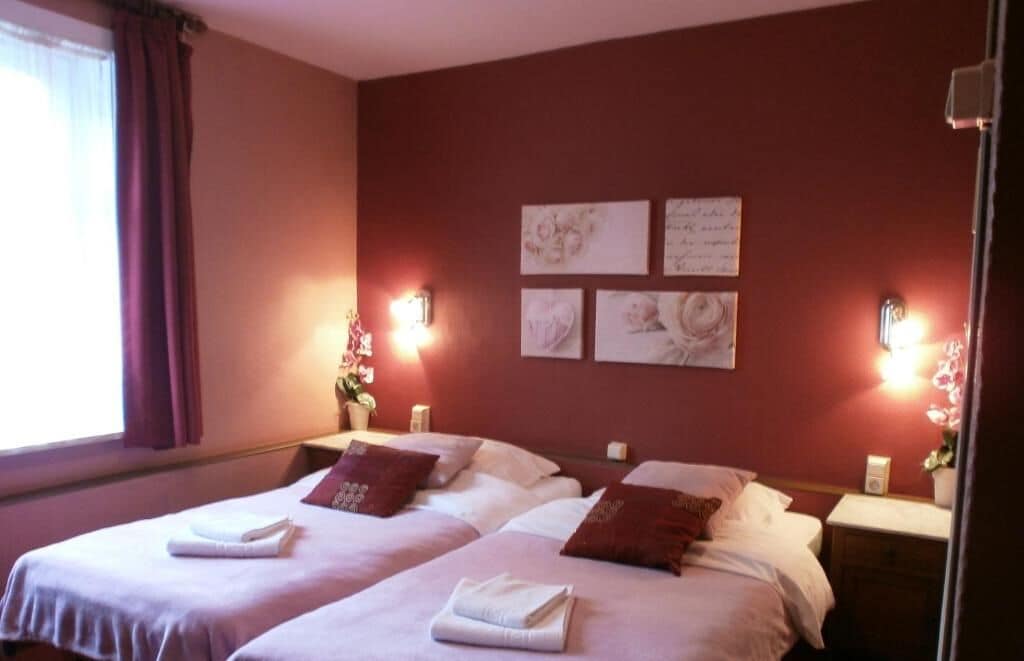 Une chambre d’hôtel avec deux lits, chacun équipé d’un oreiller et d’une serviette pliée. Des lampes murales et des œuvres d’art sont disposées au-dessus des lits.