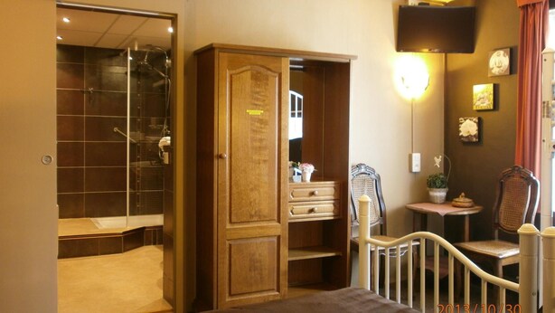 A bedroom with a large bed, a wardrobe, a mirror, a small table with a plant, and a chair. - Hotel Cobut (Onhaye)