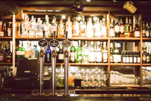 Un espace bar doté de plusieurs robinets et d’étagères remplies de diverses bouteilles et de différents types de verres.