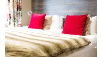 Een bed met een wit en beige deken, twee rode kussens en een bloemig gordijn op de achtergrond.