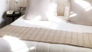 Un dormitorio con cama, mesita de noche con lámpara, y luz empotrada en la pared.