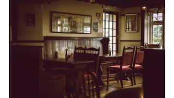 A dimly lit room with a wooden table and chairs, a large painting on the wall, and a window with multiple panes.