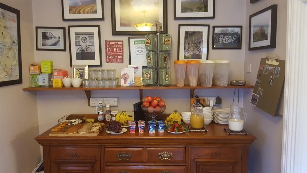 A breakfast bar with various food items and beverages, framed pictures on the wall, and a sign about sleeping in the kitchen.