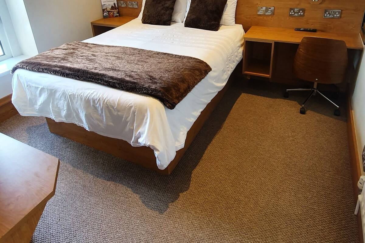 Ein Hotelzimmer mit einem großen Bett, einem Holztisch, einem Stuhl und einem an der Wand befestigten Fernseher.