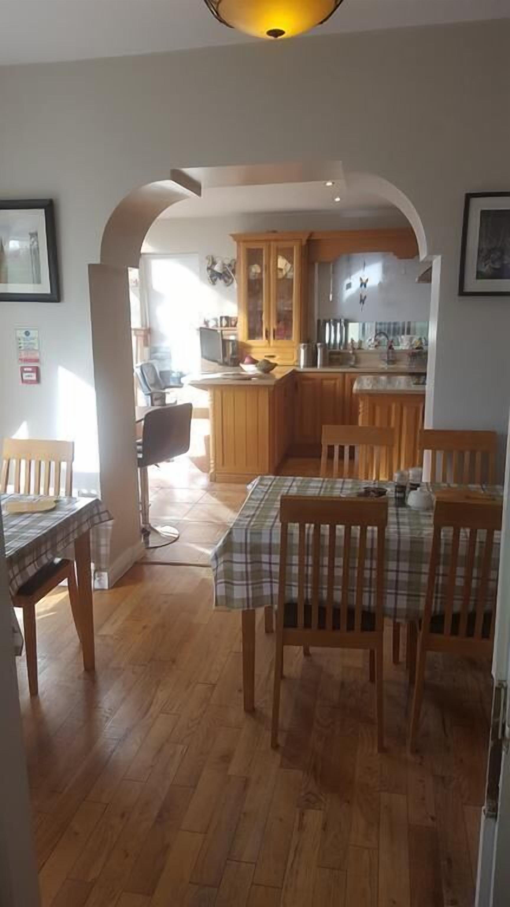 A dining area with a wooden table and chairs, a kitchen in the background, and a hallway leading to another room.