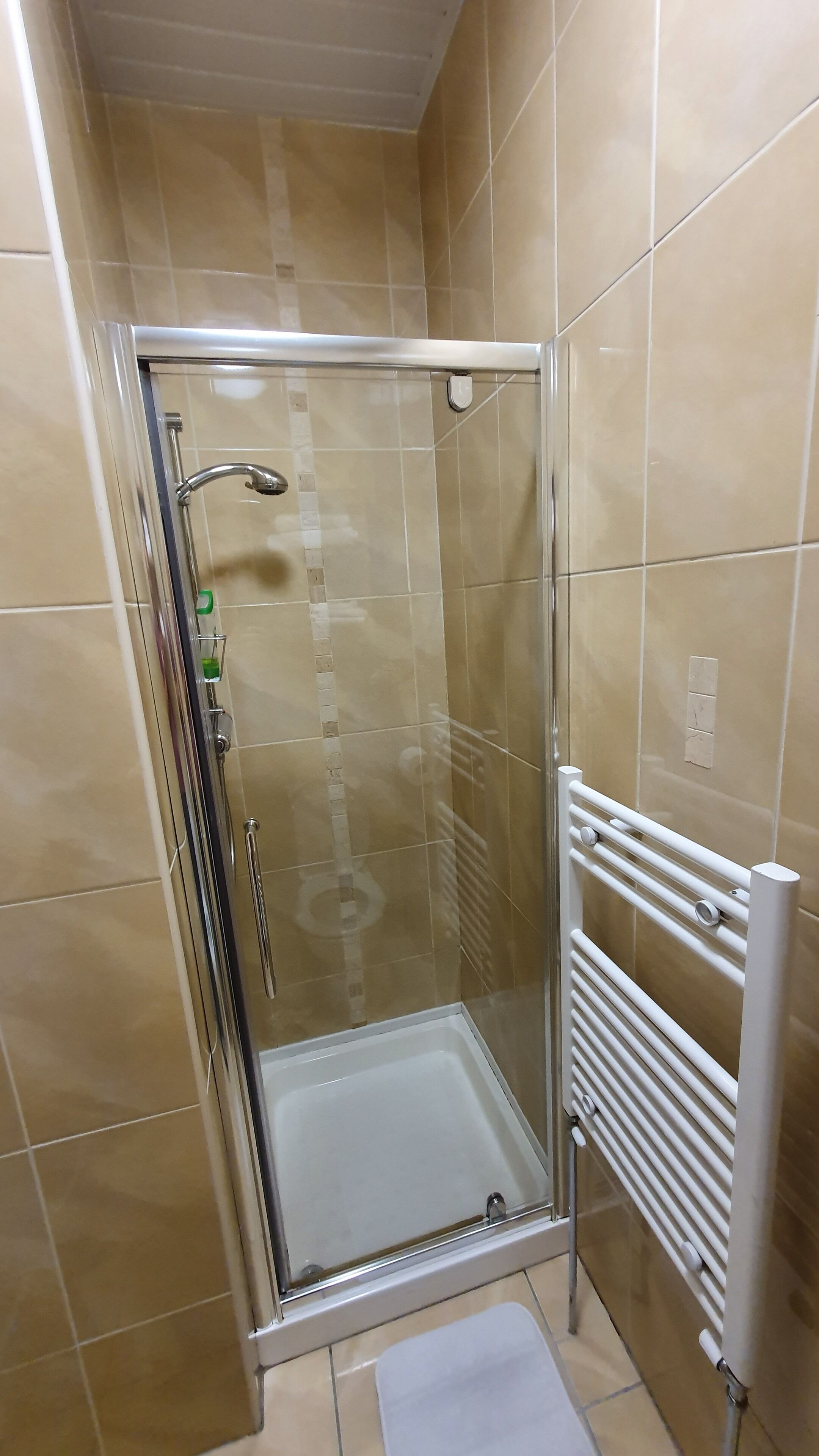 Ducha con cerramiento de vidrio, suelo blanco, puerta de vidrio y un perchero blanco a un lado.