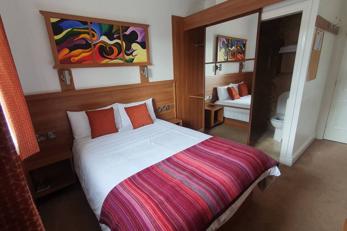 Ein Hotelzimmer mit einem großen Bett, einem Holzkopfteil, zwei Bildern an der Wand und einer Tür zu einem Badezimmer.