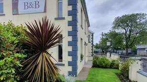 Un edificio con un letrero que indica Rose Park House B&B, que presenta un jardín con diversas plantas y una cerca de hierro negro al frente.