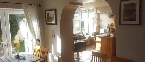 A dining area with a table set for two, a chair, and a view through an archway to a kitchen area.