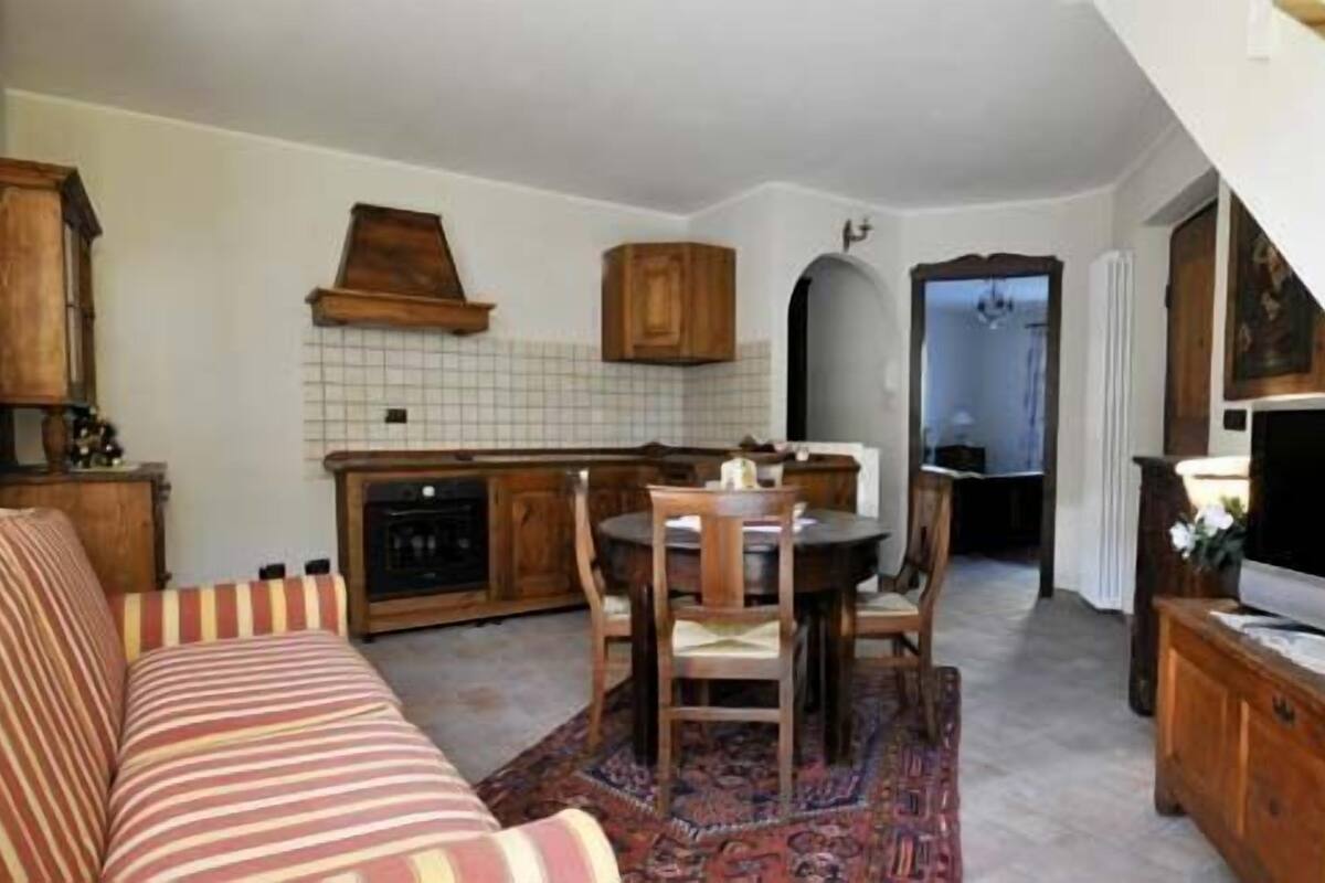 A cozy living room with a sofa, a dining table with chairs, a TV, and a kitchen area with cabinets and a tiled backsplash.