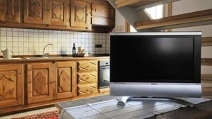Een keuken met houten kasten, een betegelde achterwand en een flatscreen televisie op een standaard.