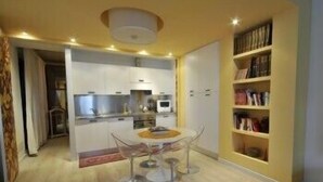 Een compacte keuken met moderne apparaten, een eethoek met een glazen tafel, en een boekenkast vol boeken.