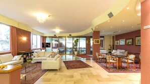A hotel lobby with a sofa, chairs, a dining table, and a large window. - Hotel Maja (Pescara)