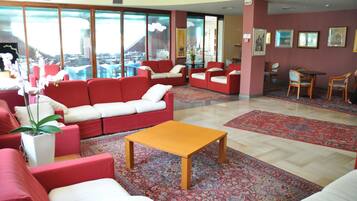 Un vestíbulo de hotel con sofás rojos, una mesa de centro de madera y un ventanal con vistas a la ciudad.