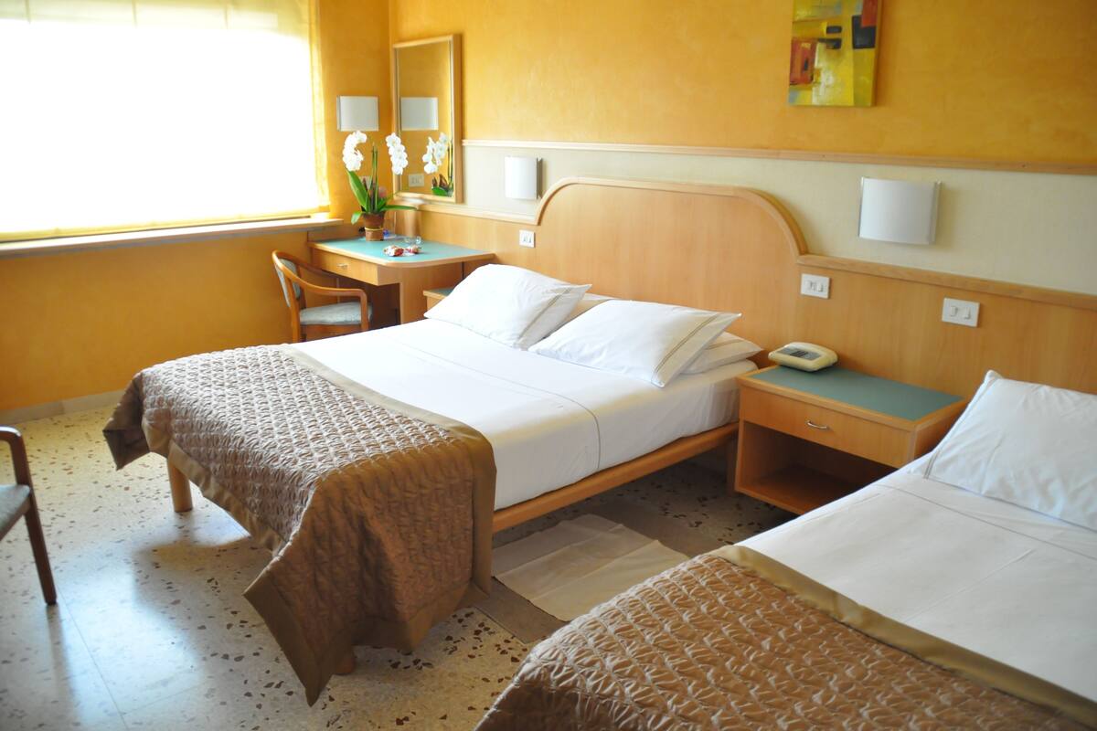 A hotel room with two beds, a desk, a chair, and a window with curtains.