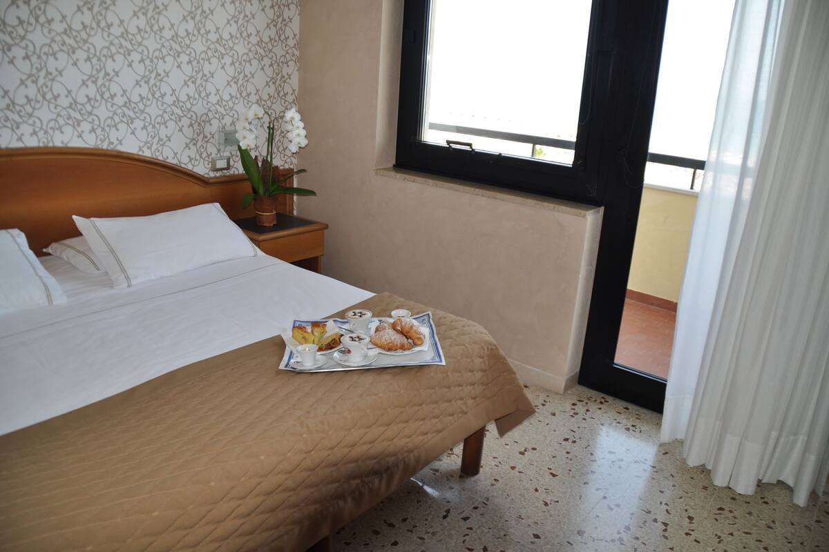 A neatly made bed with a tray of pastries and a small vase of flowers on a nightstand.
