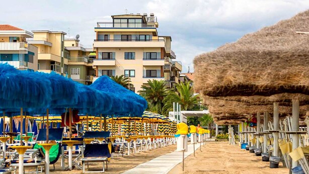 A beachside hotel with multiple floors, beach umbrellas, and thatched umbrellas. - Hotel Maja (Pescara)