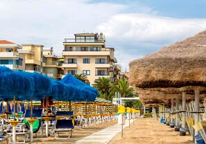 Un hôtel situé en bord de mer, avec plusieurs étages, des parasols de plage et des parasols en feuilles de palmier.