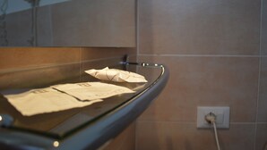 A glass display case with papers and a folded item, a light switch, and a wall with tiles. - Hotel Arena (Verona)