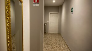 A hallway with a terrazzo floor, a gold-framed mirror, and a fire exit sign. - Hotel Arena (Verona)