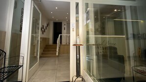 A hotel lobby with a glass wall, a black doormat with a logo, a staircase, and a small table with a sign. - Hotel Arena (Verona)