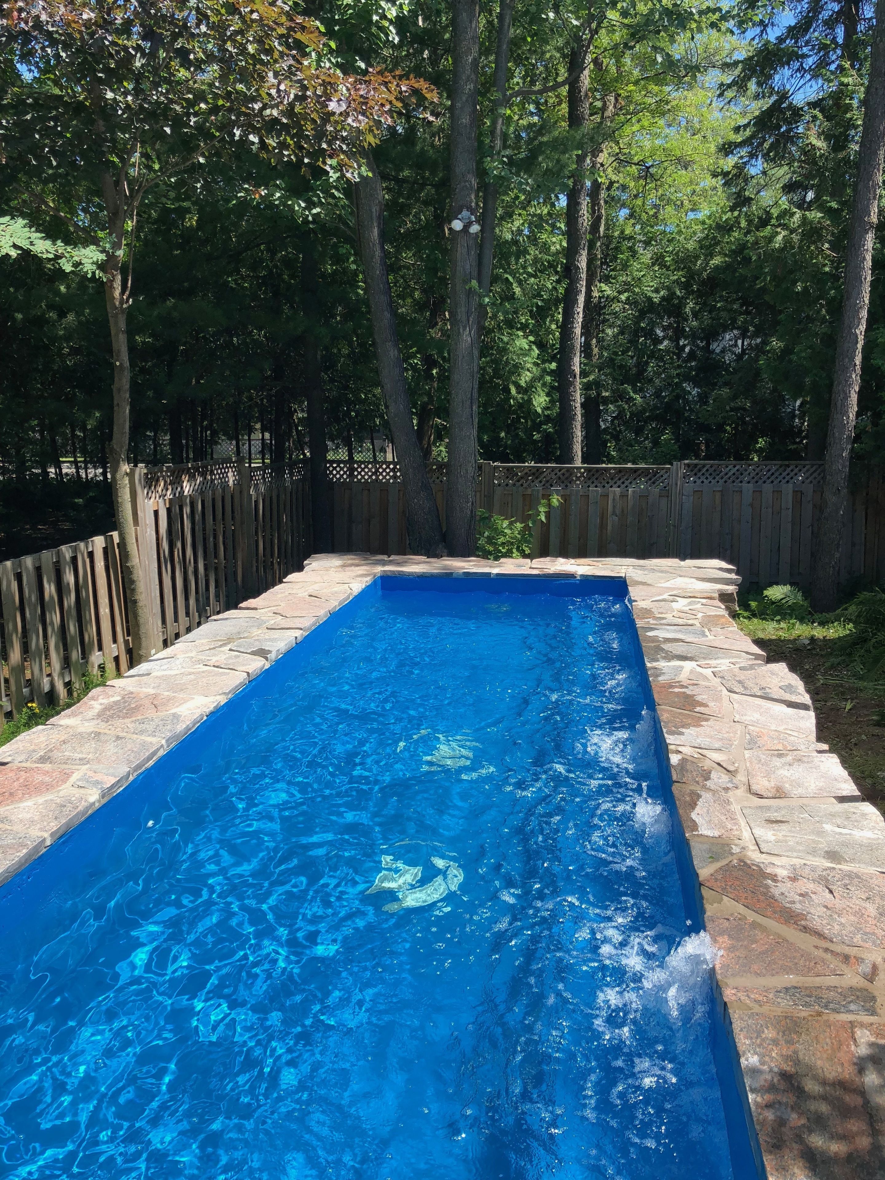 Piscina rectangular con agua azul cristalina, rodeada por un borde de piedra y una valla de madera.