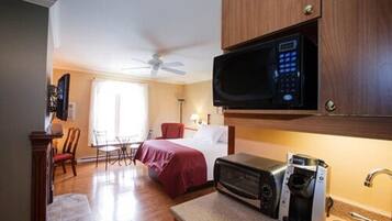 A hotel room with a bed, a microwave, a coffee maker, a ceiling fan, and a dining area with a table and chairs.