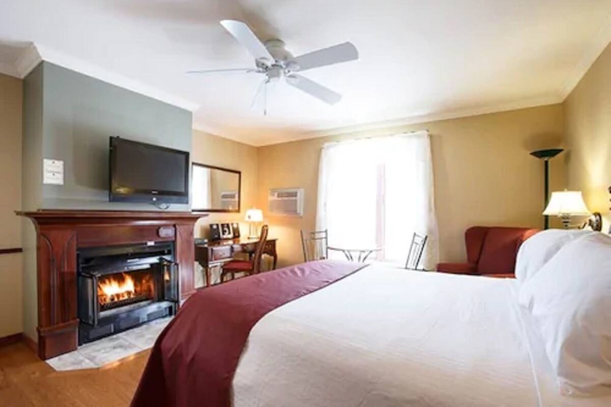 A hotel room with a fireplace, a bed, a desk, and a television.
