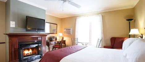 A hotel room with a fireplace, a bed, a desk, and a television.