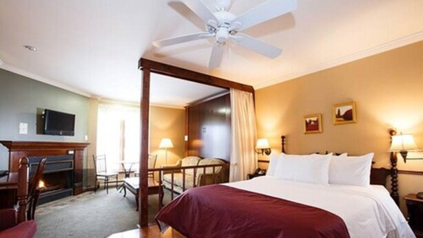 Una habitación de hotel con una cama con dosel, una chimenea, un televisor y un comedor con mesa y sillas.
